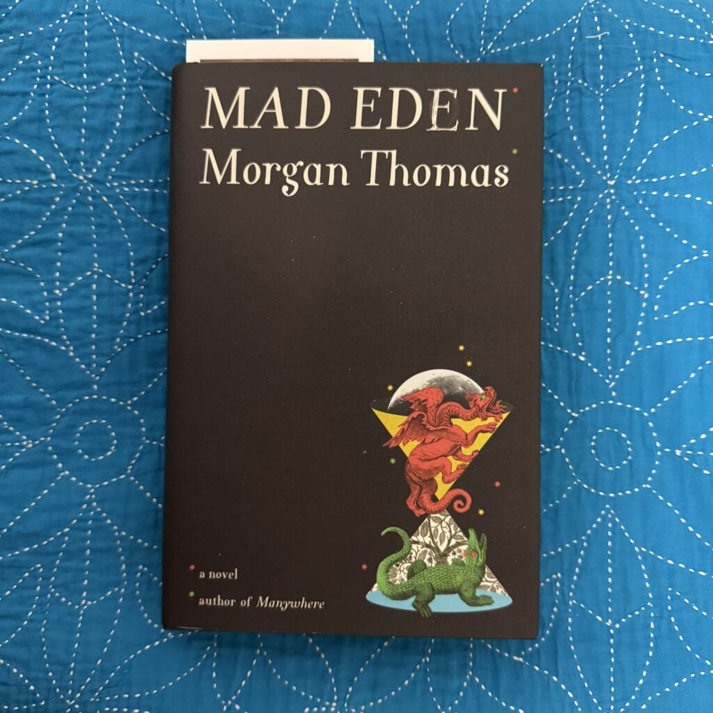 A photo showing my copy of Mad Eden by Morgan Thomas on a blue patterned cloth. The book's front cover is facing the camera.