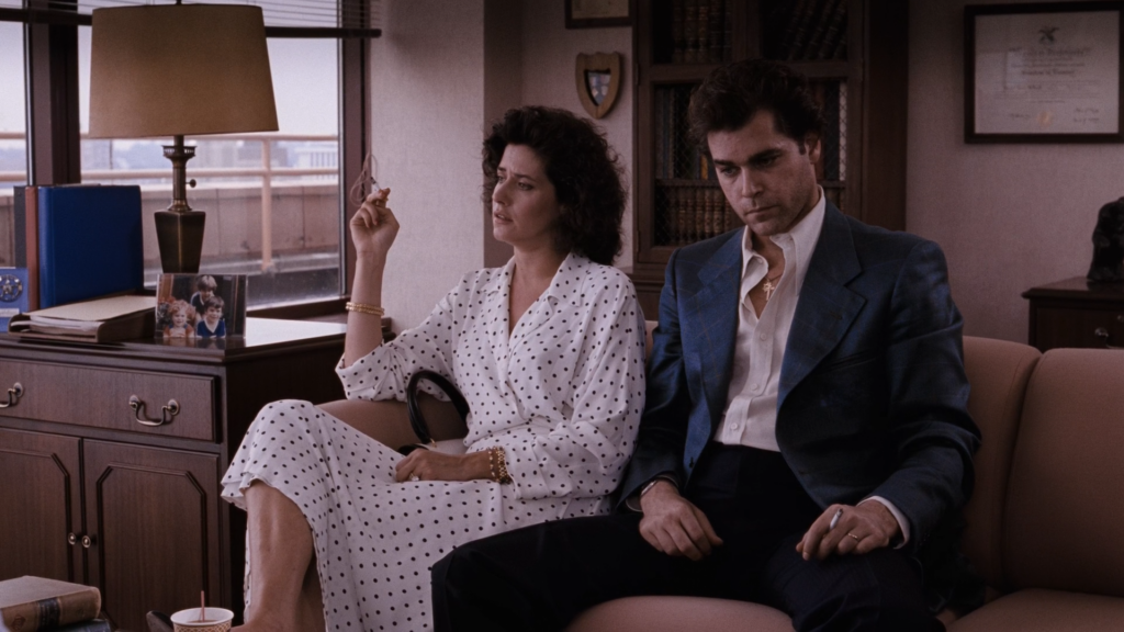 A screenshot from GoodFellas showing Henry and his wife Karen sitting on a couch in the EDNY prosecutor's office. They are both smoking cigarettes and looking dejected.