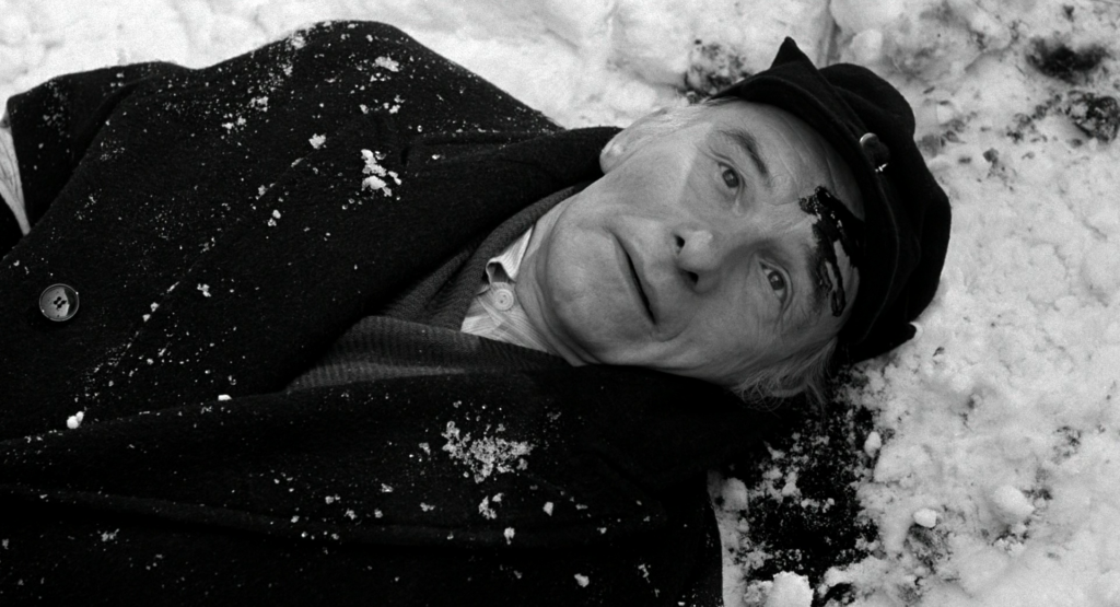 A screenshot from Schindler's List showing the one-armed Jewish machinist lying dead in the snow with blood coming out of the gunshot wound in his head.
