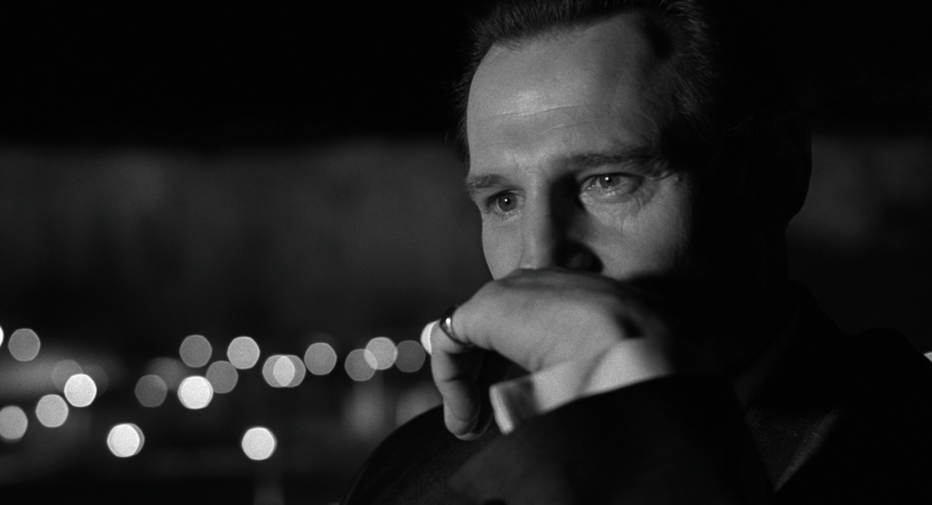 A screenshot from Schindler's List showing the main character Oskar Schindler with his left hand over his mouth pondering something.