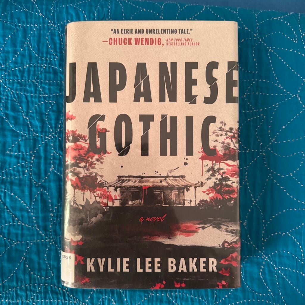 Picture of a hardcover copy of Japanese Gothic by Kylie Lee Baker sitting on a blue cloth surface with the front cover facing the camera.